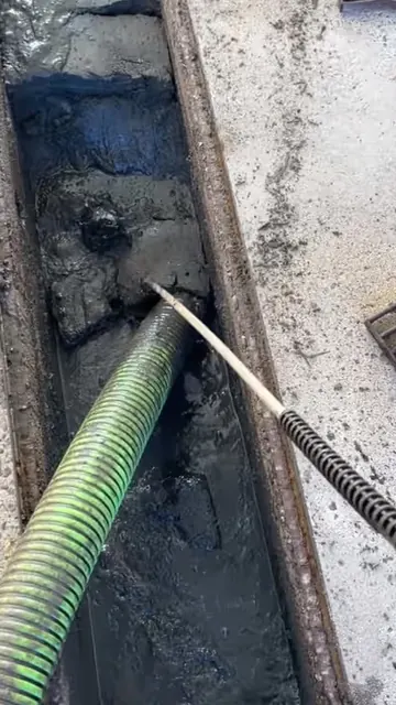 Vacuum hose clearing sludge from a car wash bay floor drain